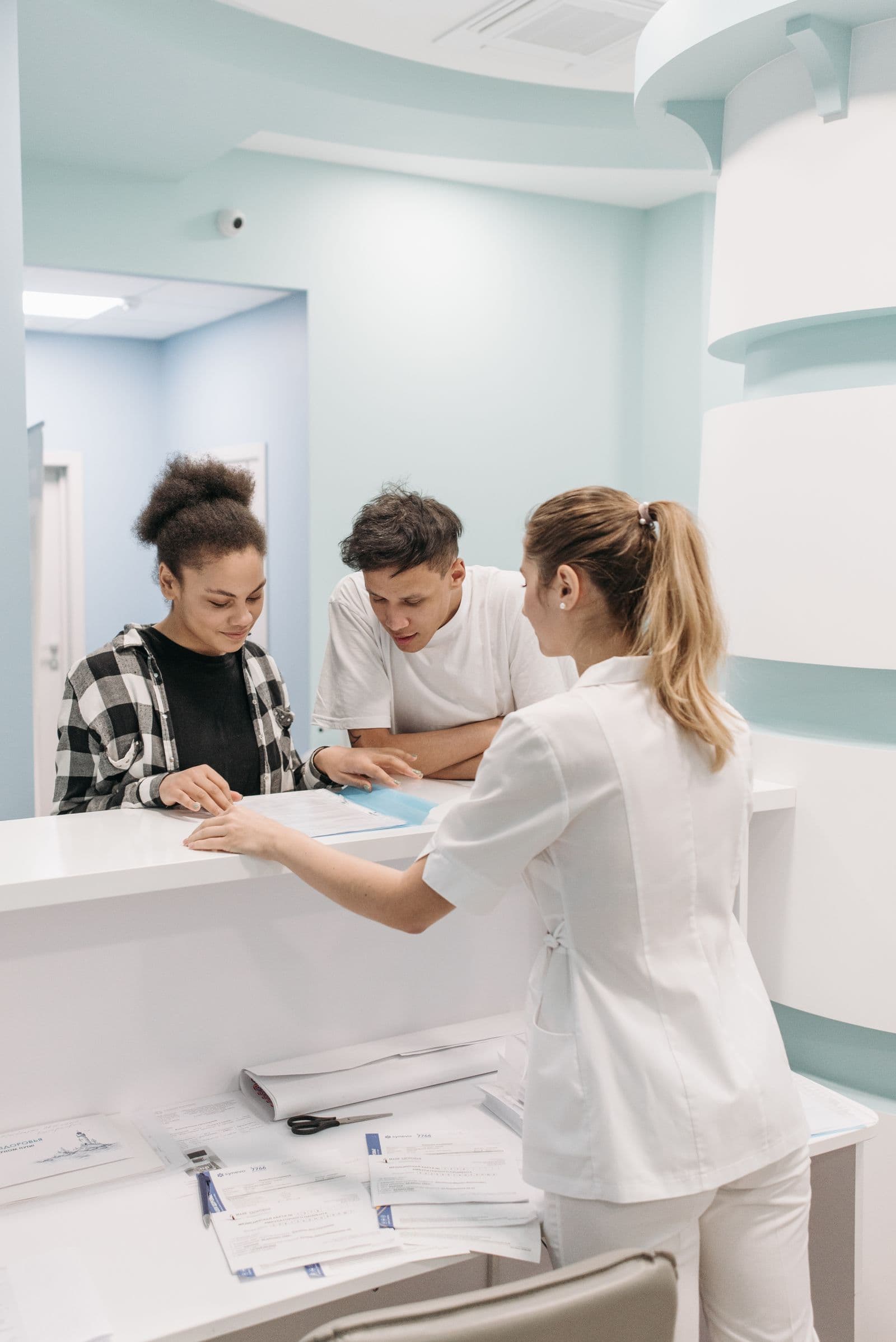 A practice team member helping two patients at the reception desk